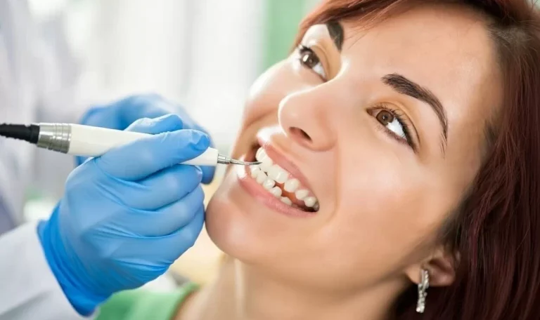 Pacientă zâmbitoare în timpul detartrajului dentar cu Airflow realizat de medic stomatolog cu mănuși albastre - clinica stomatolgoica Dental CATTED.